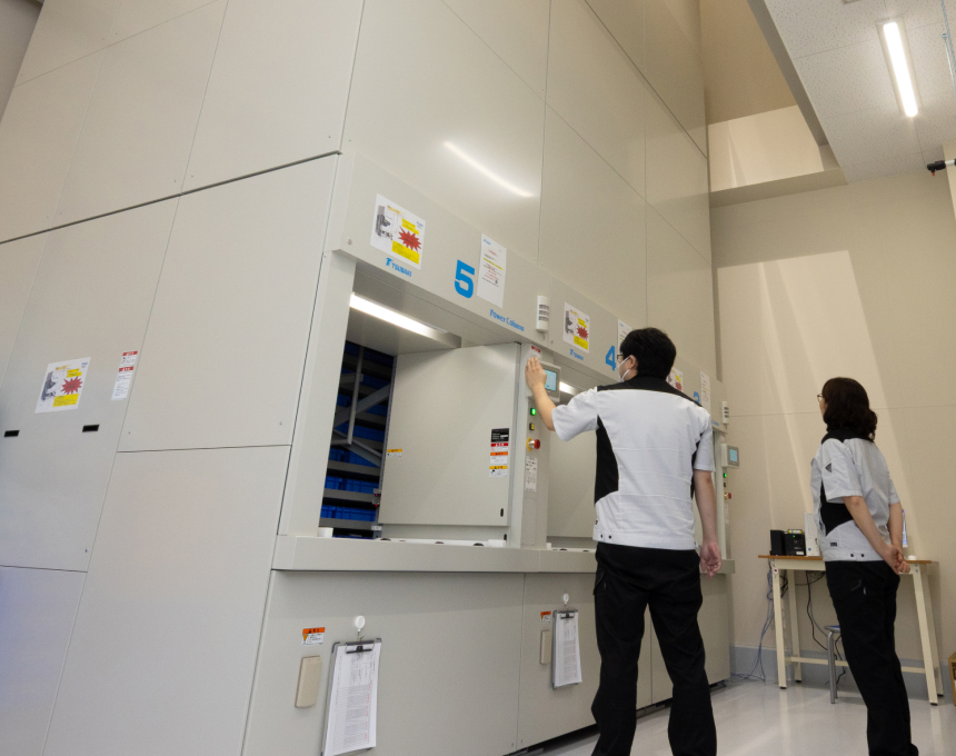 クリーンな工場内で大型自動収納庫のタッチパネルを操作する社員
