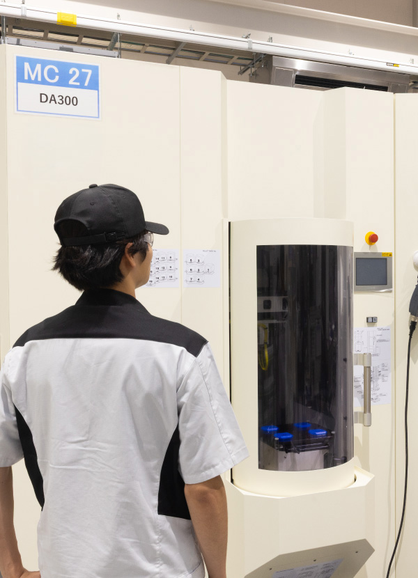 白を基調とした明るく清潔な工場内で、それぞれの設備や作業台に向かい作業に取り組む社員たち